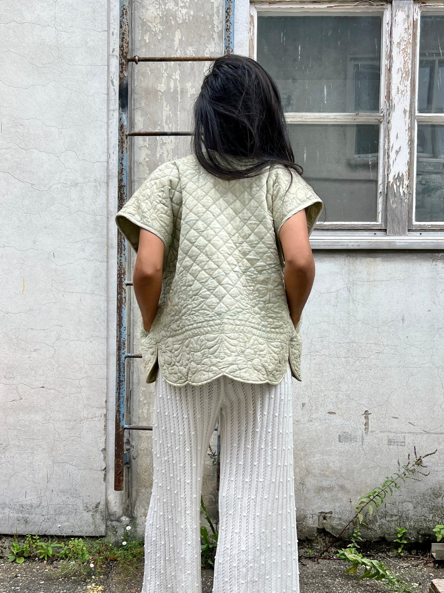 Woman wearing a light green vest in front of an old building with windows