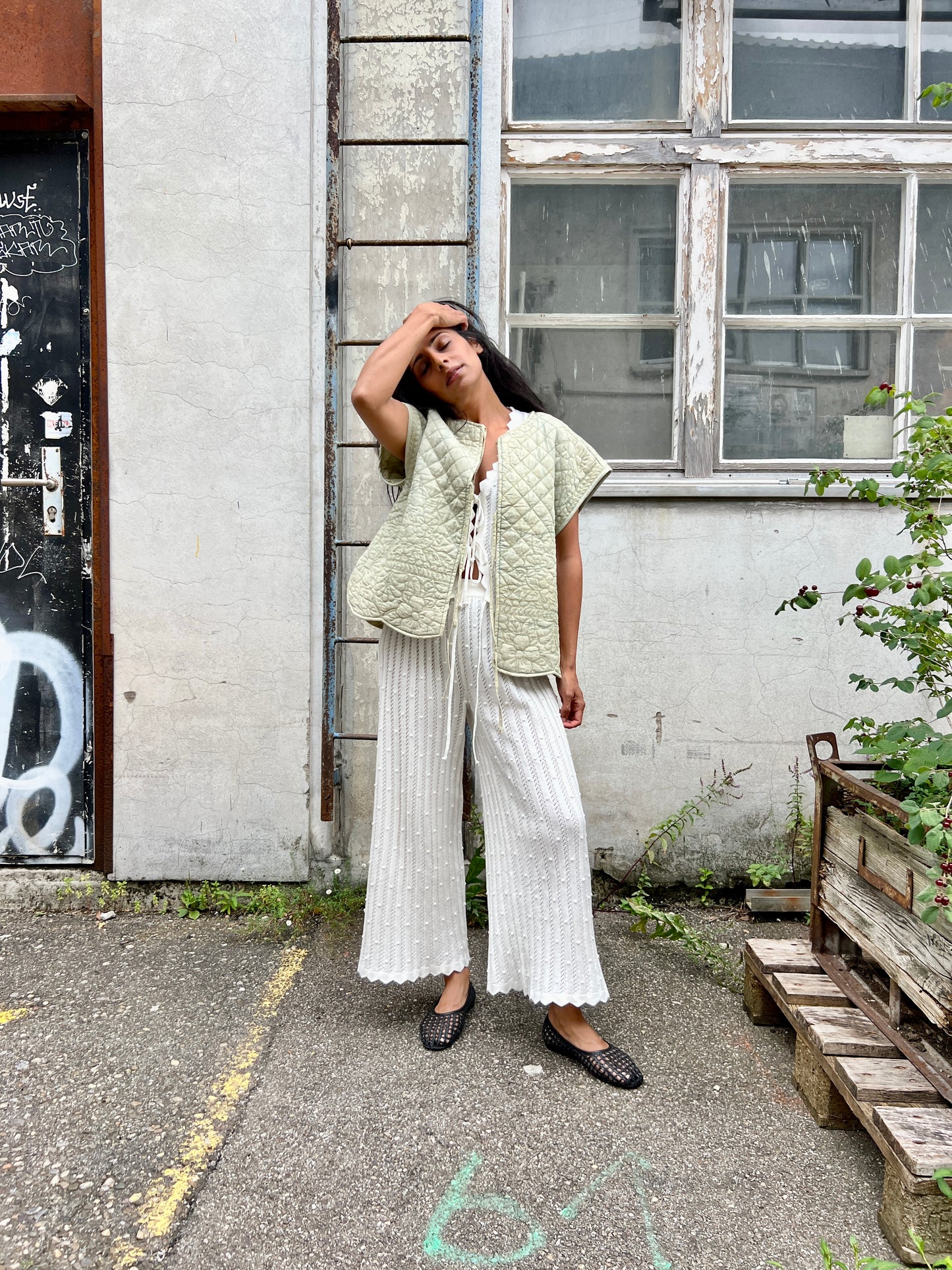 Woman wearing a light green vest over a white top and wide-leg pants, standing in an urban setting.