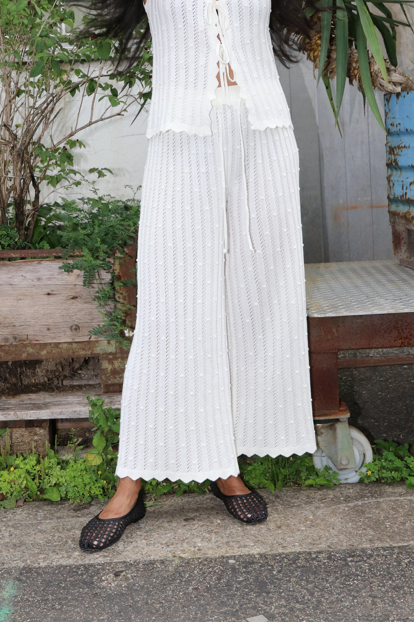 Woman wearing white knitted trousers in an industrial setting with green plants