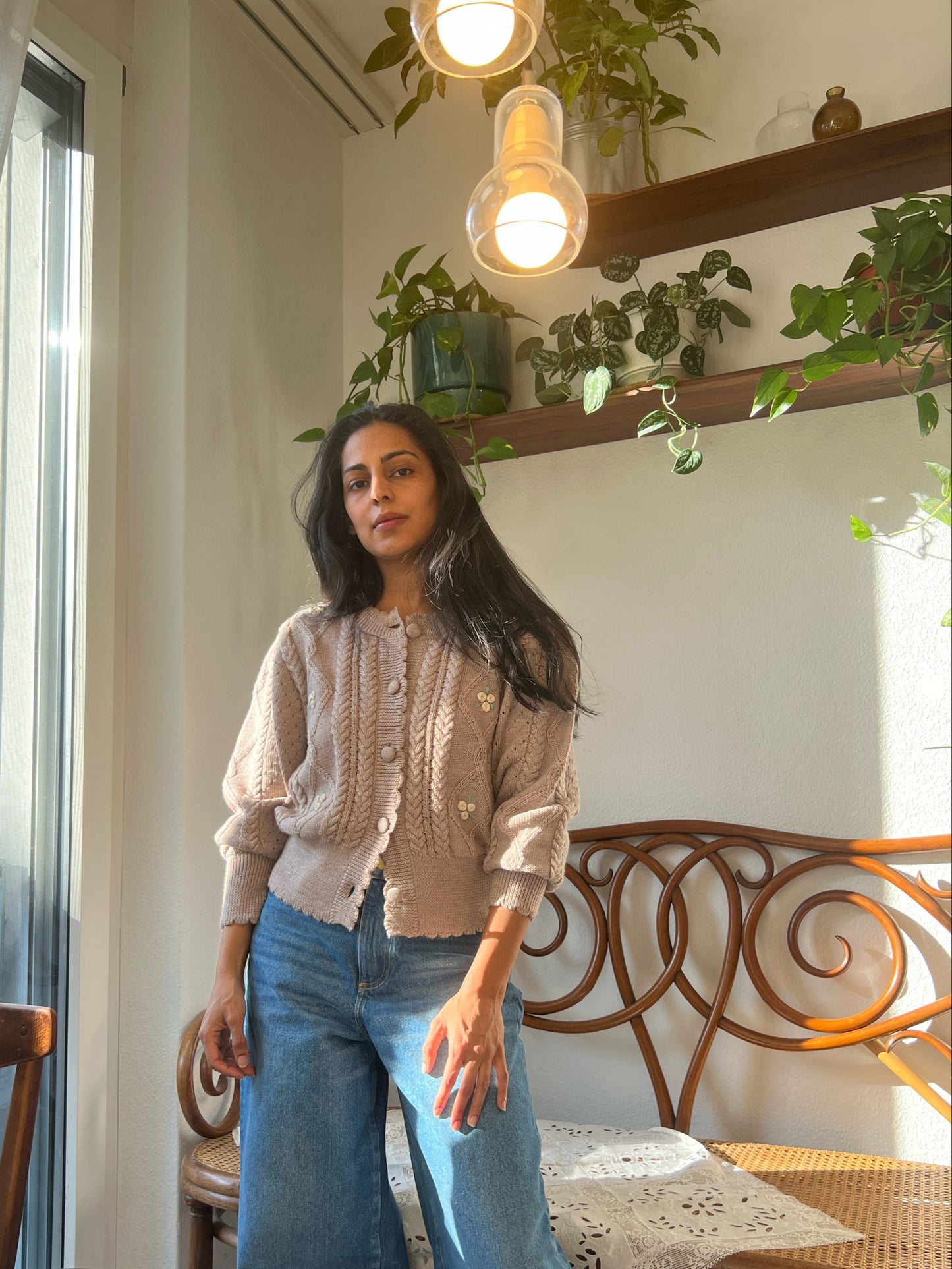 Woman wearing a Sienna Cardigan made of organic merino wool, featuring cable knit and puff sleeves, in a cozy living space.