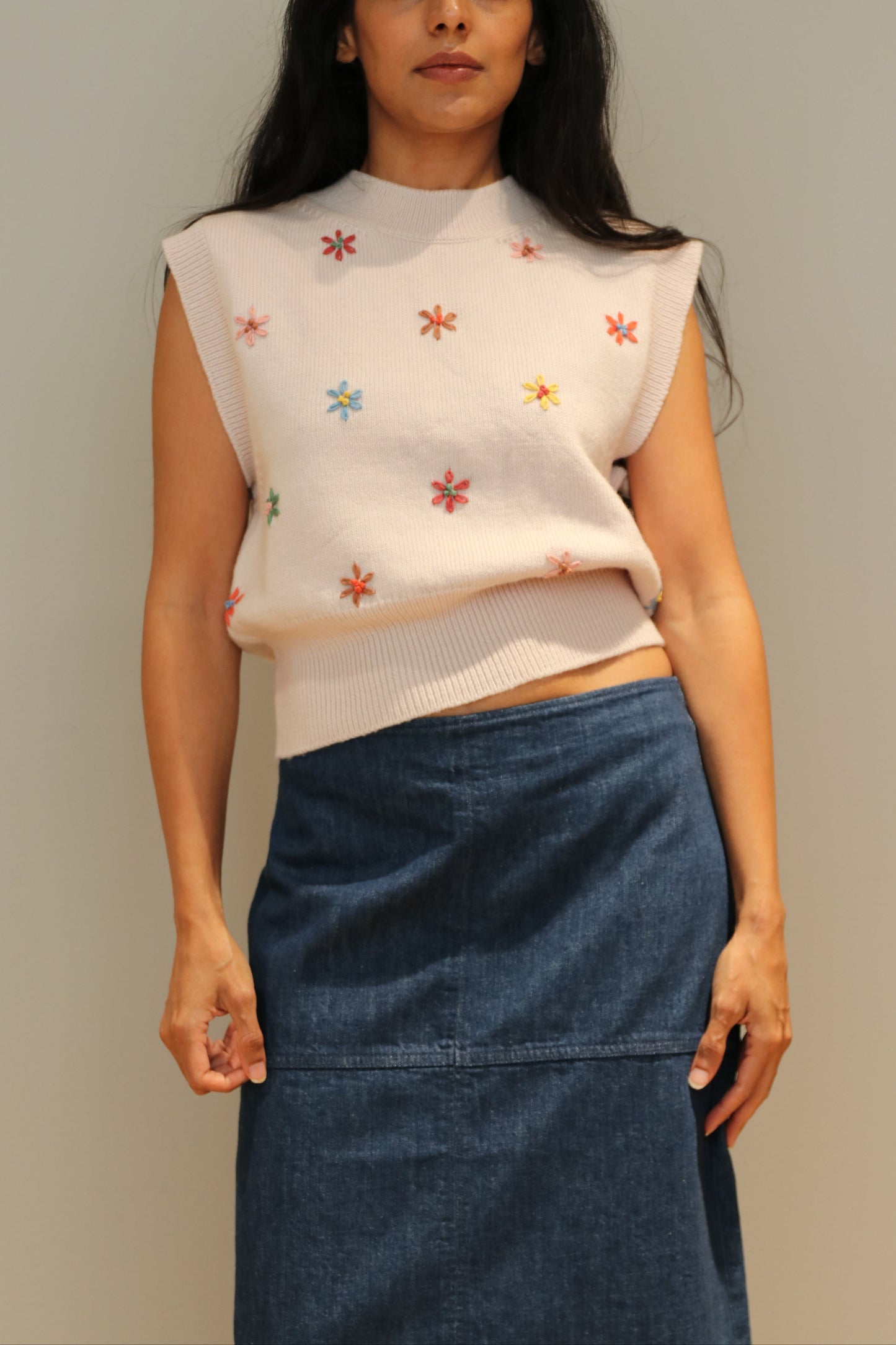 Woman wearing a white top with colorful floral patterns and a blue skirt on a plain background