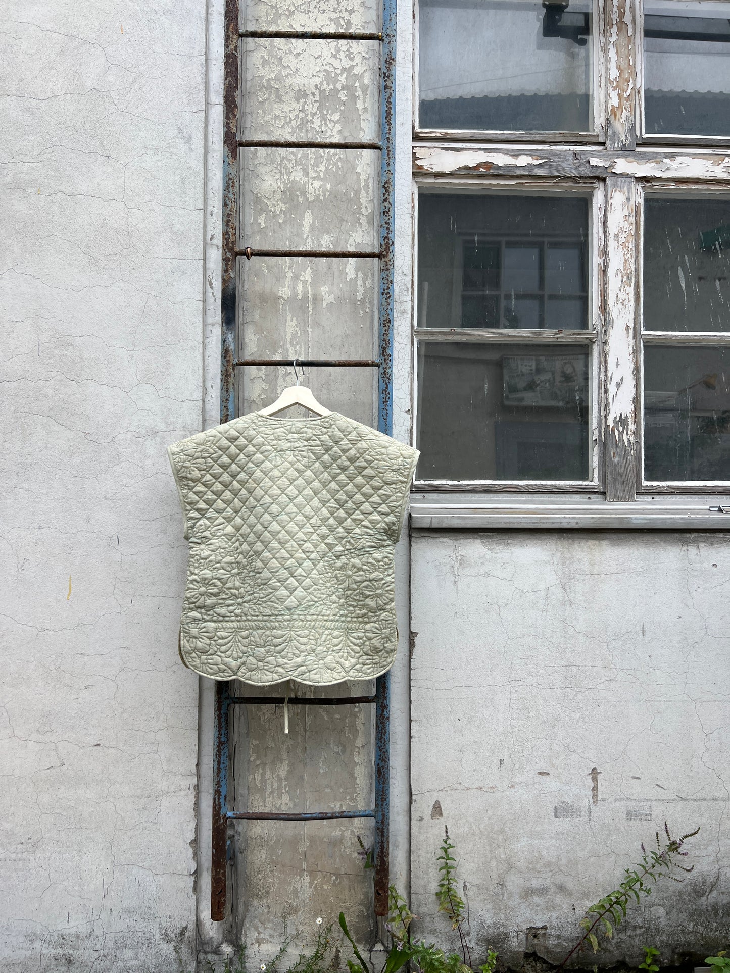Green quilted vest hanging on a ladder with a window and wall in the background