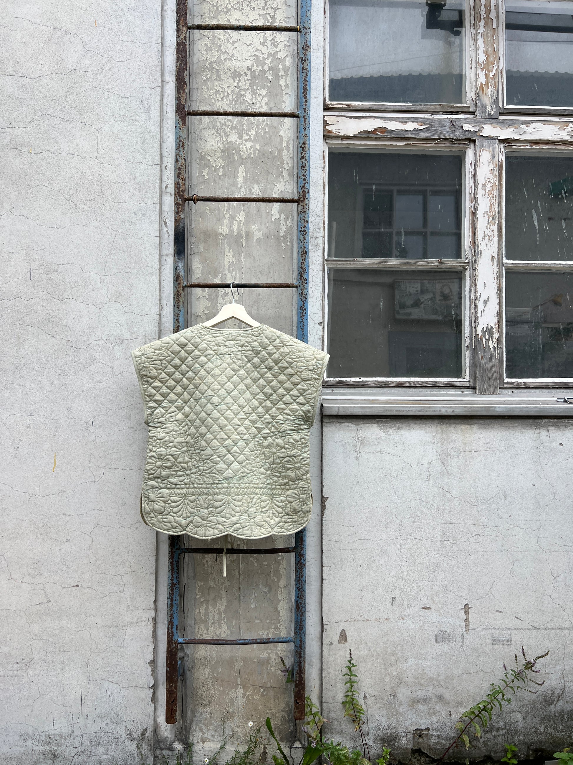 Green quilted vest hanging on a ladder with a window and wall in the background