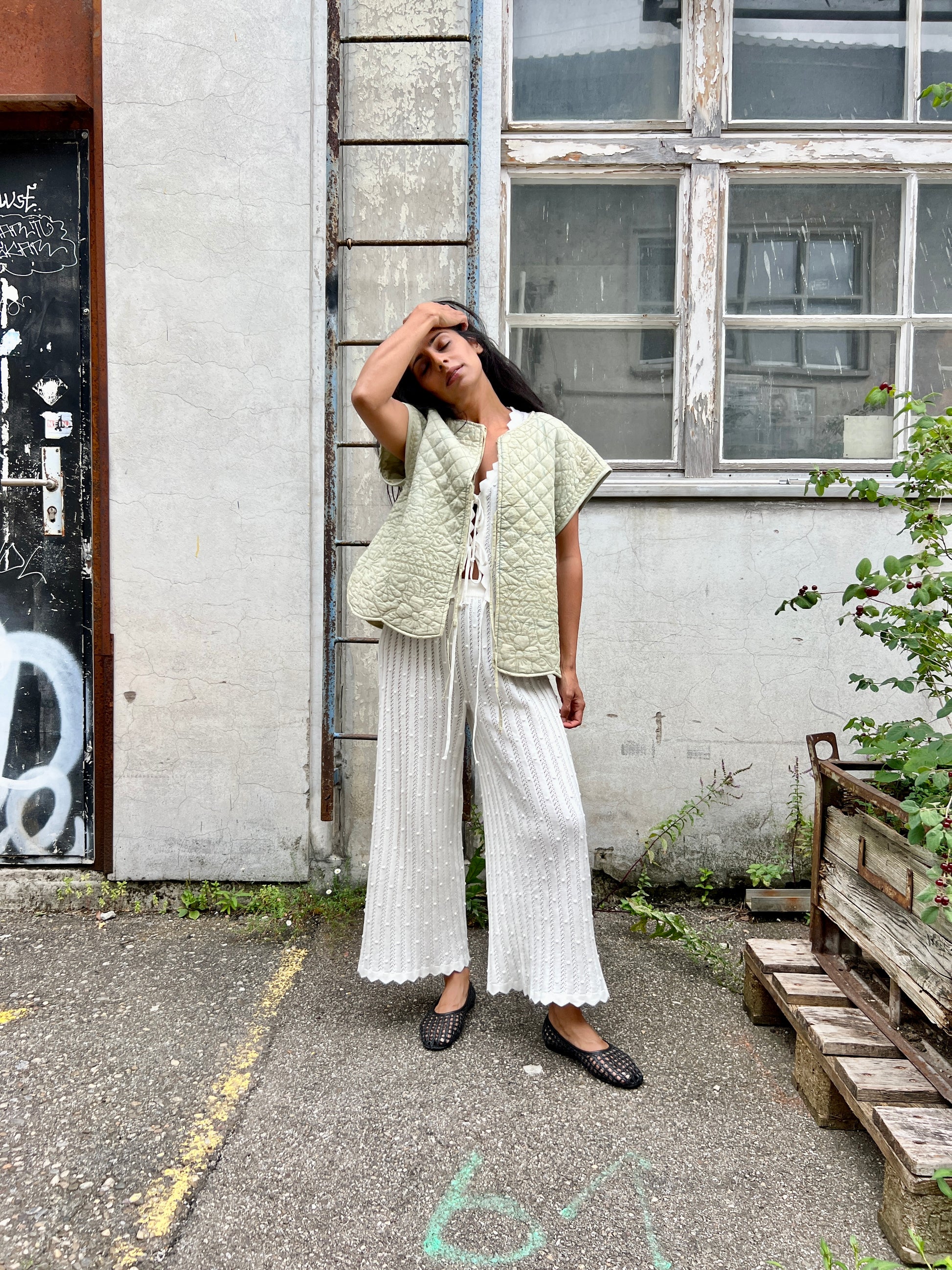Woman wearing a light green vest over a white top and wide-leg pants, standing in an urban setting.