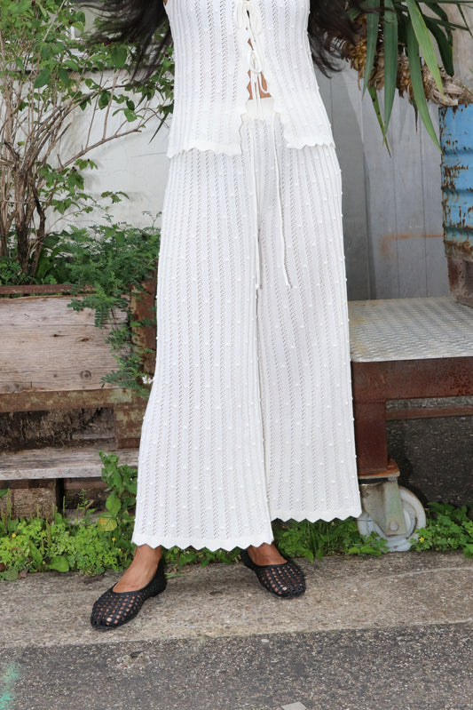 Woman wearing white knitted trousers in an industrial setting with green plants