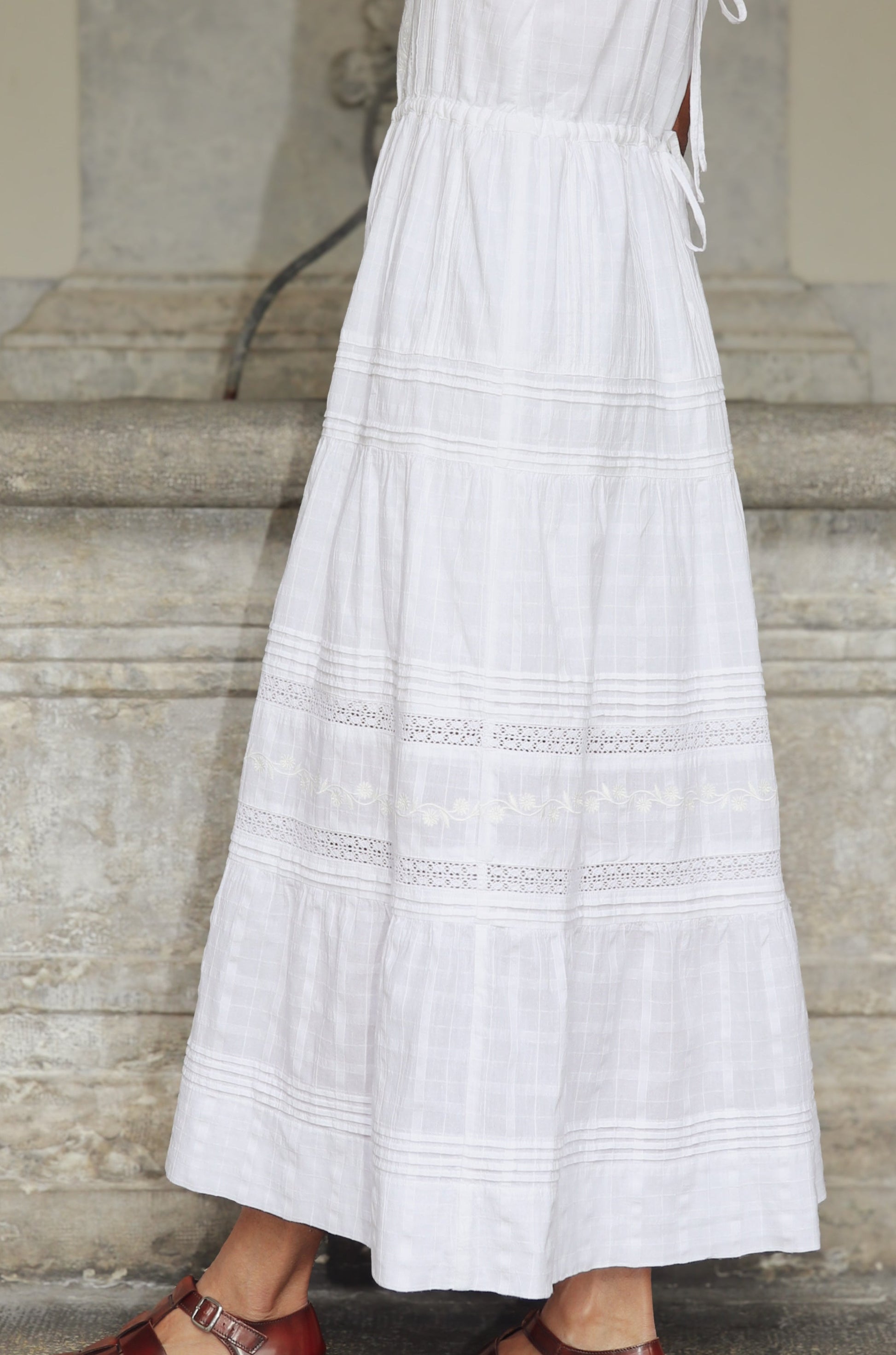 Woman in a white dress standing on stone steps with a neutral background