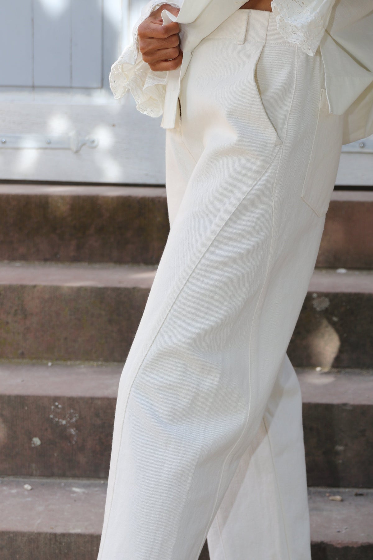 A person wearing off-white wide-leg trousers and dark brown leather sandals, standing on outdoor stone steps.