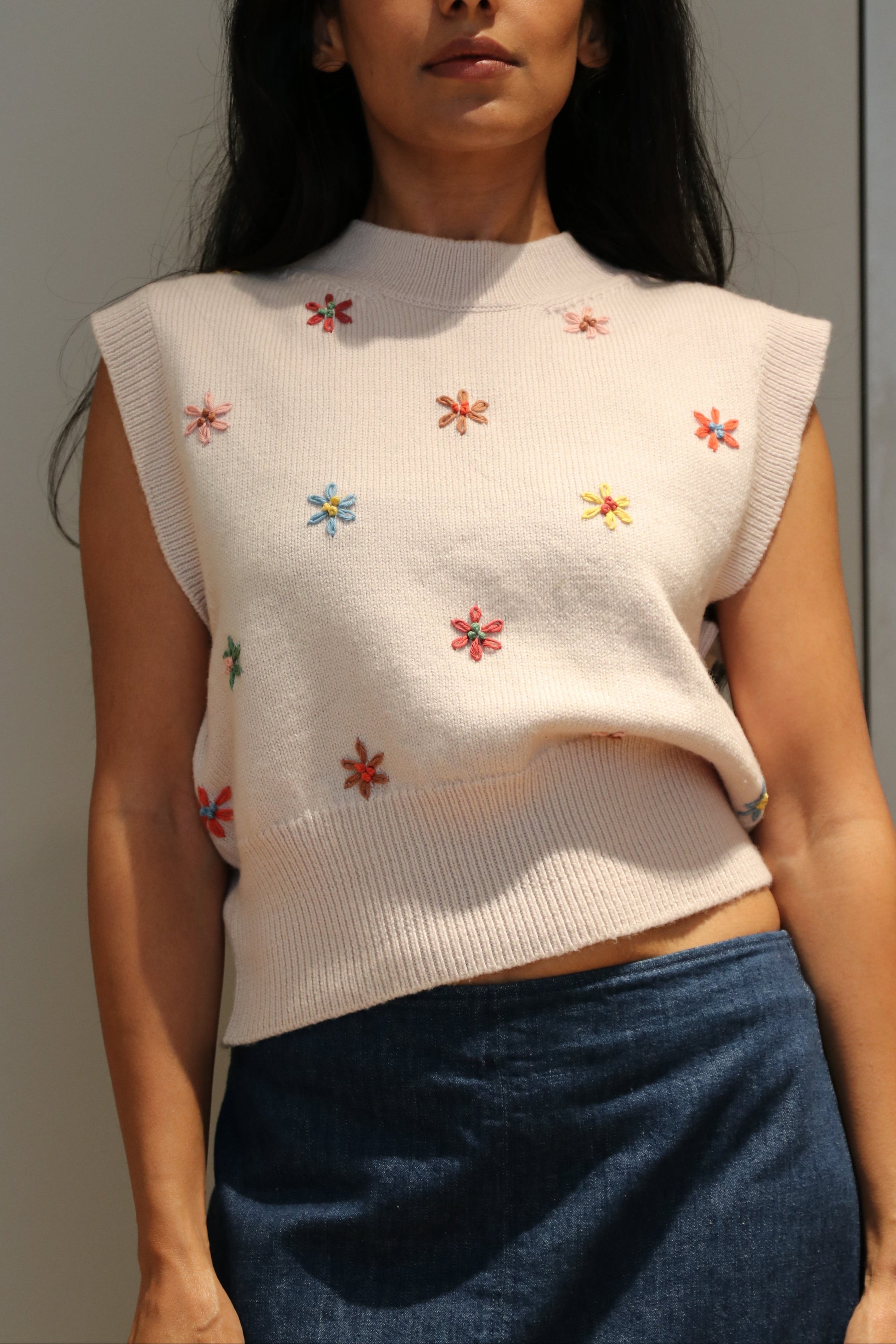 Woman wearing a white embroidered top with colorful flowers against a neutral background