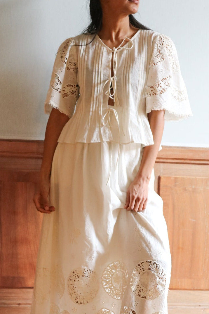 Woman in a white embroidered dress standing in a room with wooden paneling.
