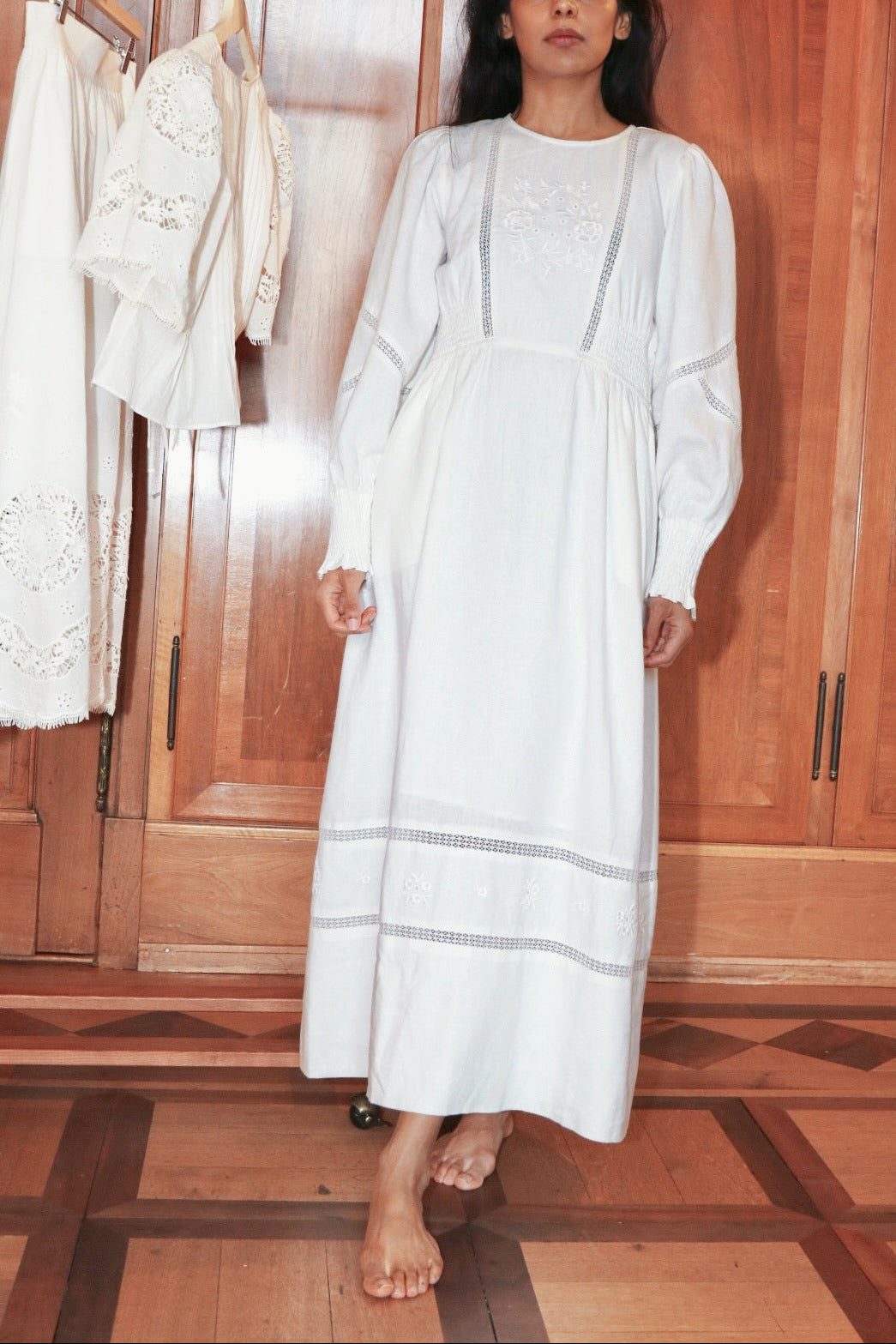 Woman in a white dress standing in a room with wooden cabinets.